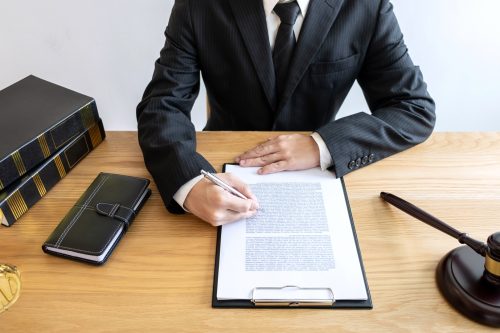 Legal law, advice and justice concept, male lawyer or notary working on a documents and report of the important case and wooden gavel, balance on table in courtroom.